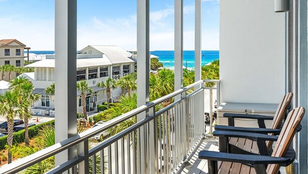 A balcony with a view of the ocean, palm trees, and buildings. - Salty's Six Palms 4A (Santa Rosa Beach)