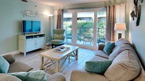 Un soggiorno con divano, tavolino, televisione e poltrona. Un balcone offre vista sul verde.