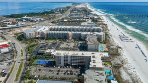 Vista aerea di una zona costiera con spiaggia, molo e complesso alberghiero con numerosi edifici e parcheggi.