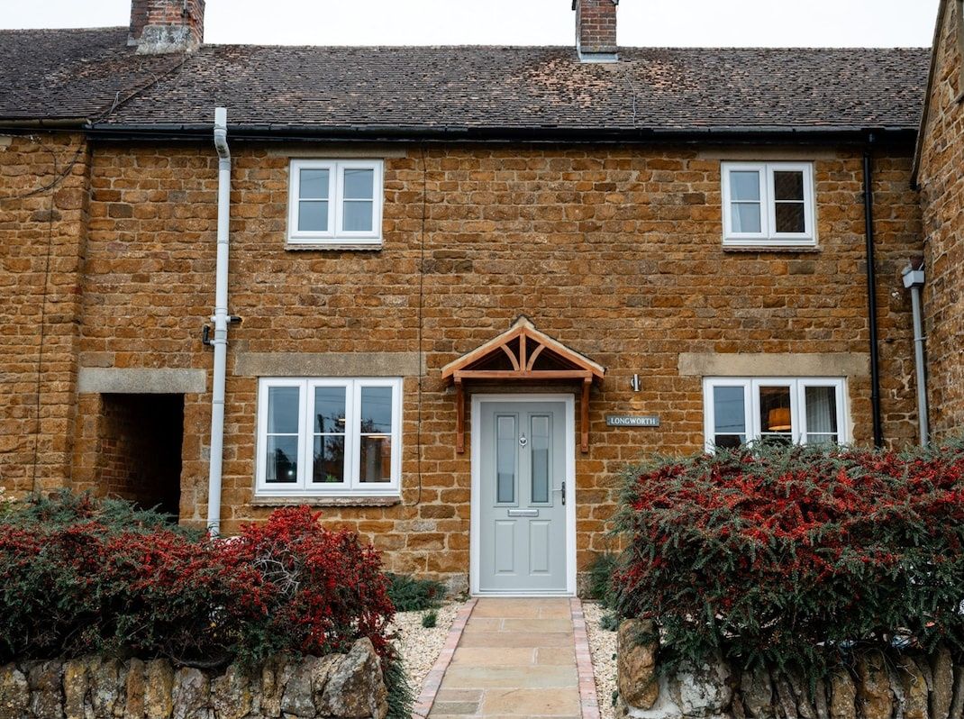 A two-story stone house with a central door, two windows on each floor, and a small porch area.