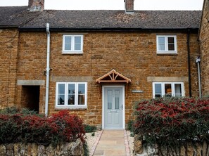 A two-story stone house with a central door, two windows on each floor, and a small porch area. - 3x Bedroom House (Sleeps 7x) (Oxfordshire)