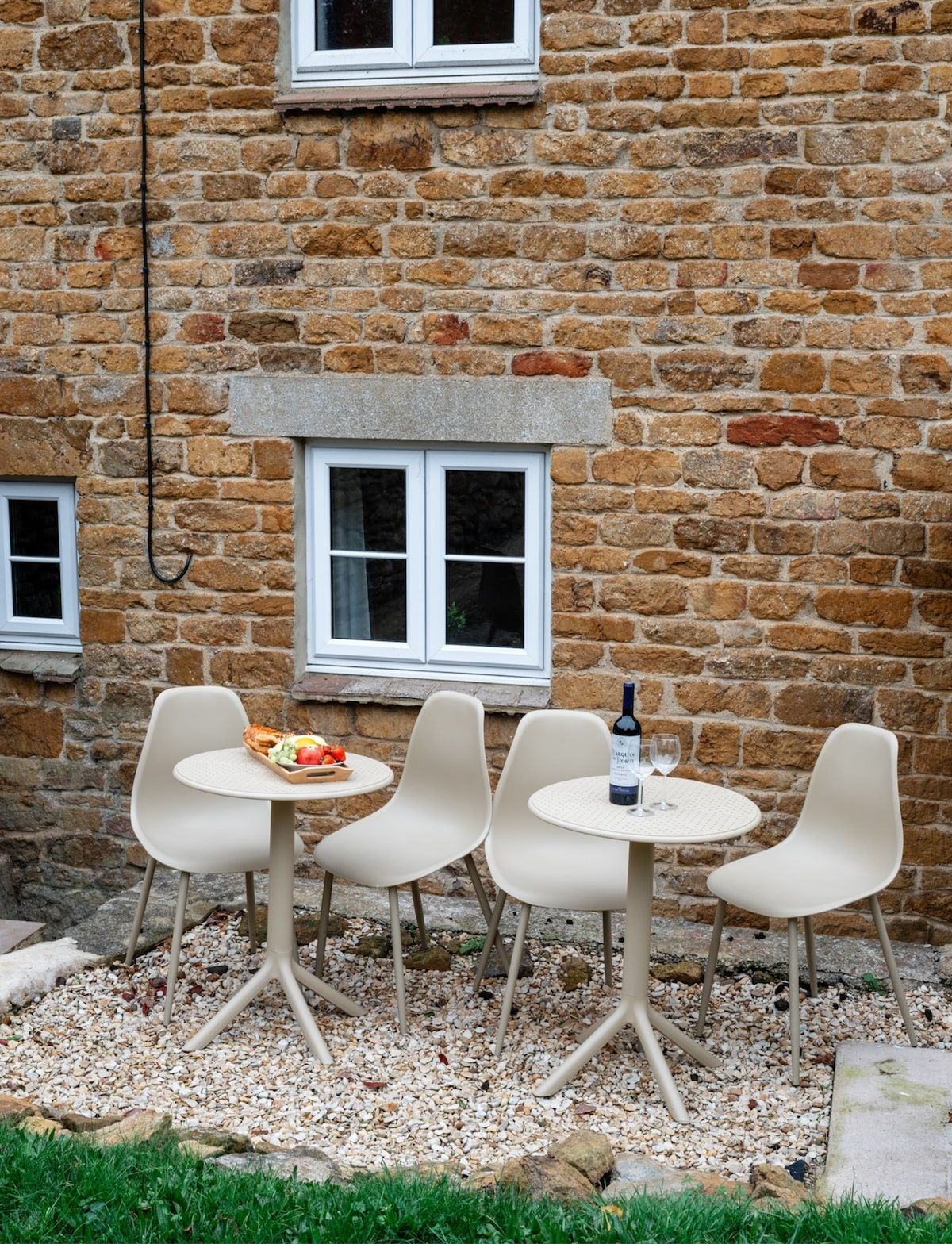 A stone building with two windows and a small table with chairs in front.
