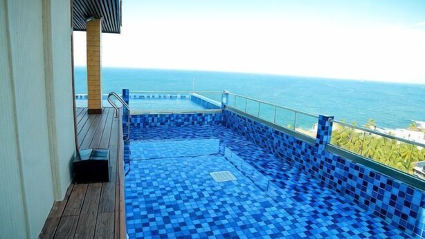 A pool with blue tiles, a wooden deck, and a view of the ocean. - Araliya Beach Resort & Spa Unawatuna- Where You Meet the Sea All Year (Unawatuna)