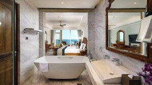 A modern bathroom with a freestanding bathtub, a large mirror, and a view of a bedroom with a bed and a window overlooking the sea. - Araliya Beach Resort & Spa Unawatuna- Where You Meet the Sea All Year (Unawatuna)