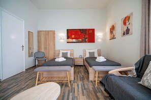 Ein Hotelzimmer mit zwei Einzelbetten, einem Sofa, einem kleinen Tisch und einem Sessel. An den Wänden befinden sich Wandleuchten und Kunstwerke.