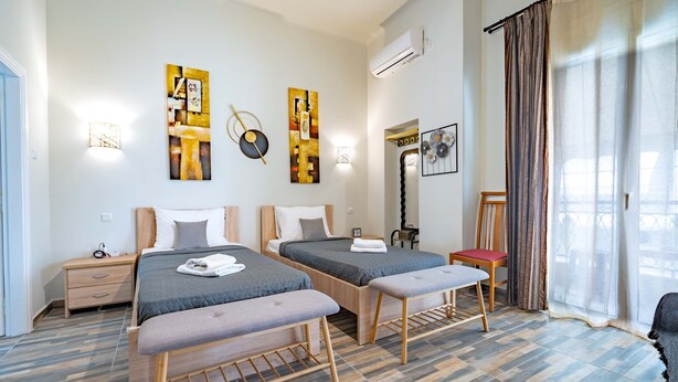 A modern bedroom with two beds, a bench, a chair, and artwork on the walls.