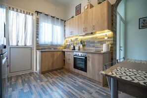 A modern kitchen with wooden cabinets, a built-in oven, and a dining area with a patterned table. - Attiki Haven – 4BR Stay • Steps from Metro by ΜΡS (Athina)