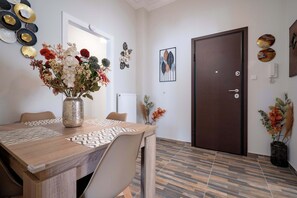 A dining area with a wooden table, chairs, and a vase of flowers. There is a door and a wall with decorative plates and a framed picture. - Attiki Haven – 4BR Stay • Steps from Metro by ΜΡS (Athina)