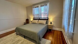 A bedroom with a bed, two bedside tables with lamps, a chair, a window with curtains, and a ceiling fan.