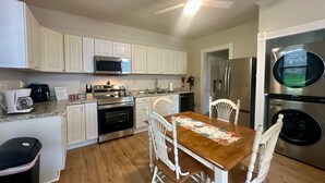 A kitchen with white cabinets, stainless steel appliances, a wooden dining table, and a ceiling fan.