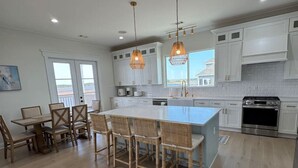 A modern kitchen with white cabinets, a central island, and pendant lighting. - New 5BR Bayfront Home | Fishing, Kayaking & Boat Launch Access (Bay St. Louis)