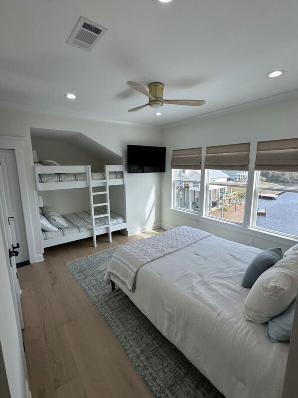 A bedroom with a bed, a ceiling fan, a TV, bunk beds, and a window with a view of the water.