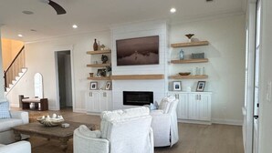 A spacious living room with a fireplace, white furniture, and wooden floors. - New 5BR Bayfront Home | Fishing, Kayaking & Boat Launch Access (Bay St. Louis)