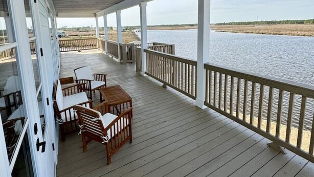 A covered deck with wooden furniture and a view of a body of water. - New 5BR Bayfront Home | Fishing, Kayaking & Boat Launch Access (Bay St. Louis)