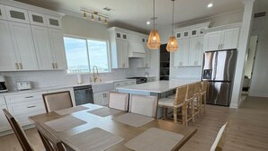 A modern kitchen with white cabinets, a large island, and a stainless steel refrigerator. - New 5BR Bayfront Home | Fishing, Kayaking & Boat Launch Access (Bay St. Louis)