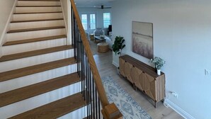 A spacious living area with a staircase leading to an upper floor, a chandelier, and a large window. - New 5BR Bayfront Home | Fishing, Kayaking & Boat Launch Access (Bay St. Louis)