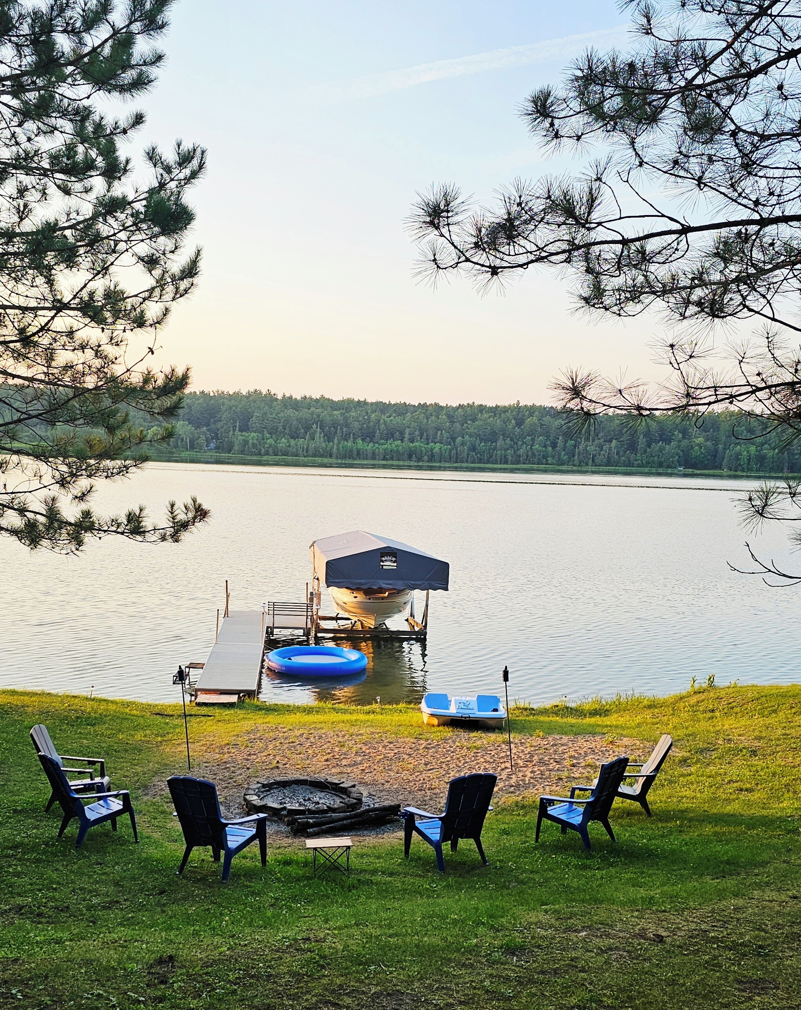 A lakeside deck with outdoor seating and a dock with a boat.