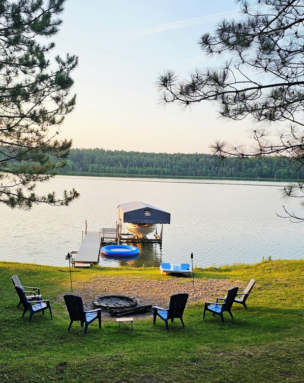 A lakeside deck with outdoor seating and a dock with a boat.