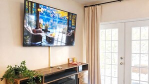 Un salon avec un téléviseur à écran plat fixé au-dessus d’un meuble de rangement en bois, une table basse en verre et un tapis bleu à motifs.