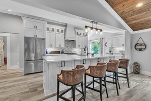 A modern kitchen with white cabinetry, a stainless steel refrigerator, and a central island with bar stools.