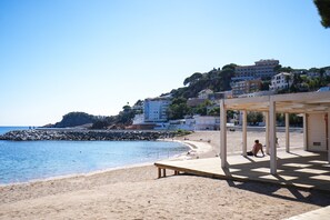 A beach with a wooden deck and a building in the background. - SJ7 Aparthotel (Sant Feliu de Guíxols)