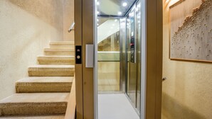 An elevator with a glass door, a control panel, and a wall-mounted artwork. - SJ7 Aparthotel (Sant Feliu de Guíxols)