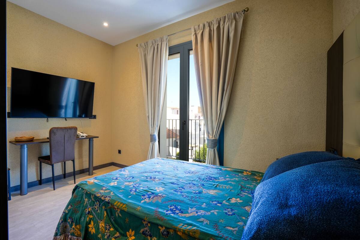 Une chambre d’hôtel comprenant un lit, un bureau avec une chaise, une télévision et une fenêtre avec des rideaux.