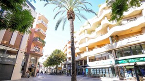 A street with palm trees, shops, and a building with balconies. - SJ7 Aparthotel (Sant Feliu de Guíxols)
