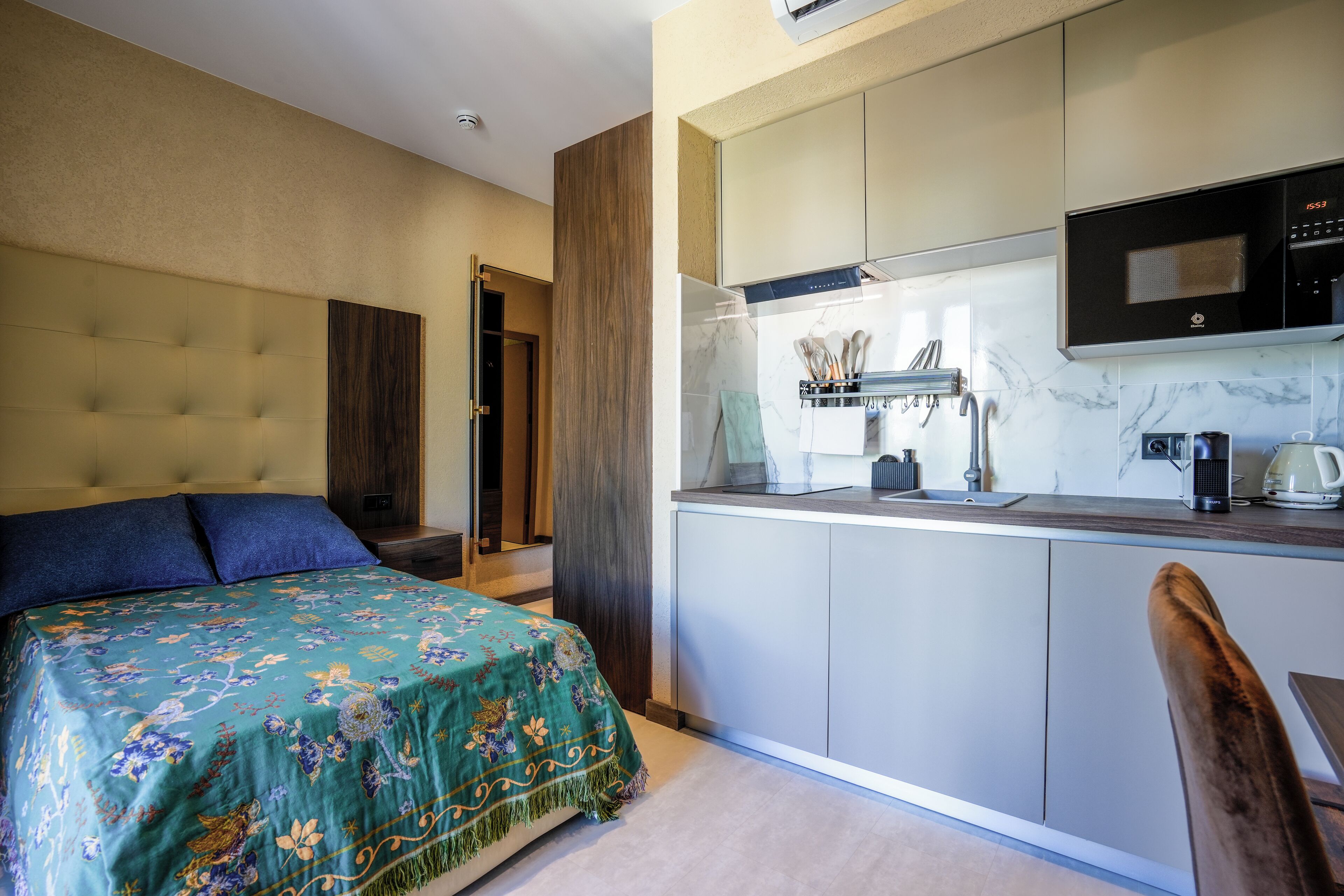 A compact hotel room with a bed, a kitchenette, and a bathroom.