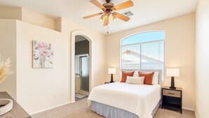 A bedroom with a bed, two bedside tables, a ceiling fan, a window with blinds, and a door leading to another room. - Near stadiums and sports complex, Peoria Oasis (Peoria)