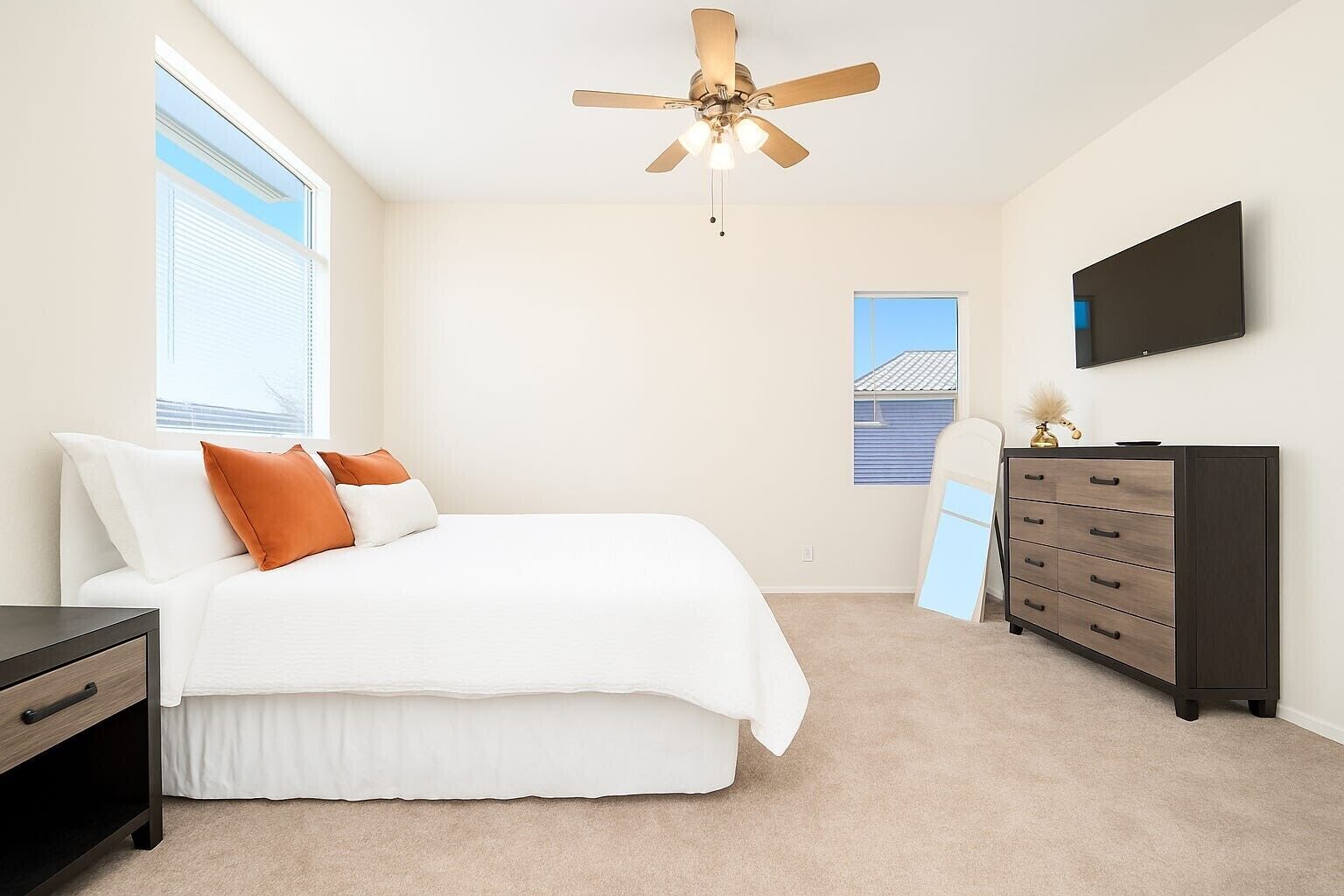 A bedroom with a bed, dresser, TV, ceiling fan, and windows.