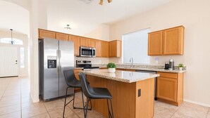 A modern kitchen with a central island, stainless steel appliances, wooden cabinets, and a large window. - Near stadiums and sports complex, Peoria Oasis (Peoria)