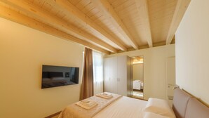 Una camera d'albergo con soffitto in legno, un letto con copriletto trapuntato, una TV a schermo piatto montata a parete e uno specchio che riflette parte della stanza.