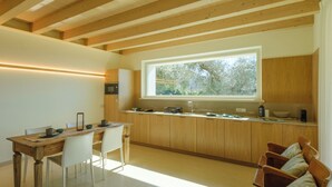 Een moderne keuken met houten balken, een eethoek met een tafel en stoelen, en een groot raam dat zorgt voor daglicht.