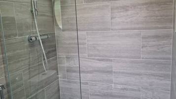 A modern bathroom with a glass shower enclosure, grey tiles, and a visible showerhead.