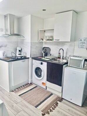 A compact kitchen with a washing machine, microwave, and sink. - Cozy studio apartment near Heathrow (Northolt)