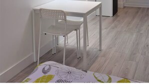 Una stanza con una finestra sul tetto, un tavolo bianco con una sedia, un orologio appeso al muro e una porta con un cartello che indica Wi-Fi gratuito.