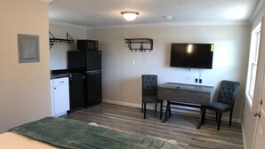 A compact room with a bed, a kitchenette, a dining area, and a TV mounted on the wall.
