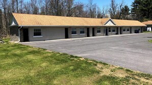 A motel with a long, single-story building, a covered parking area, and a grassy front yard.