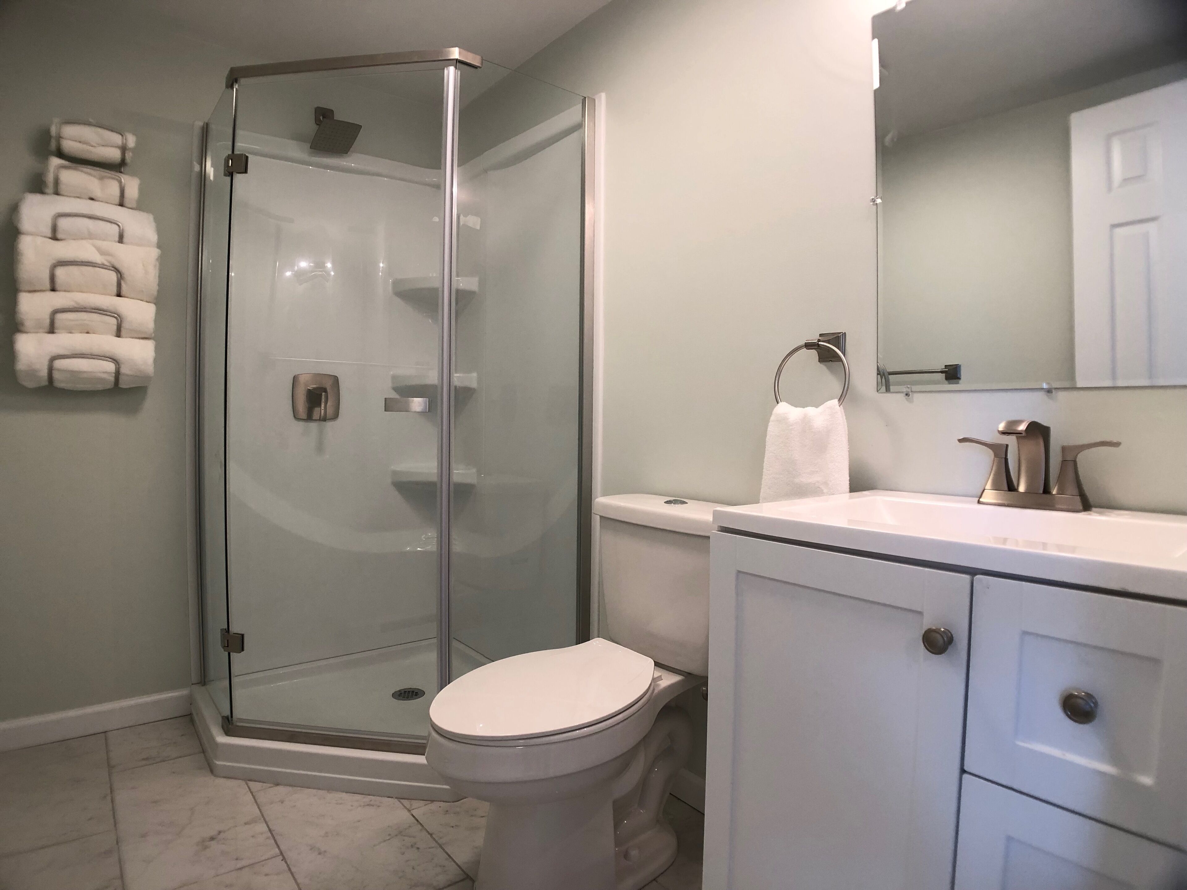 Een moderne badkamer met een douche met glazen wand, een toilet en een wastafel met handdoekhouder.