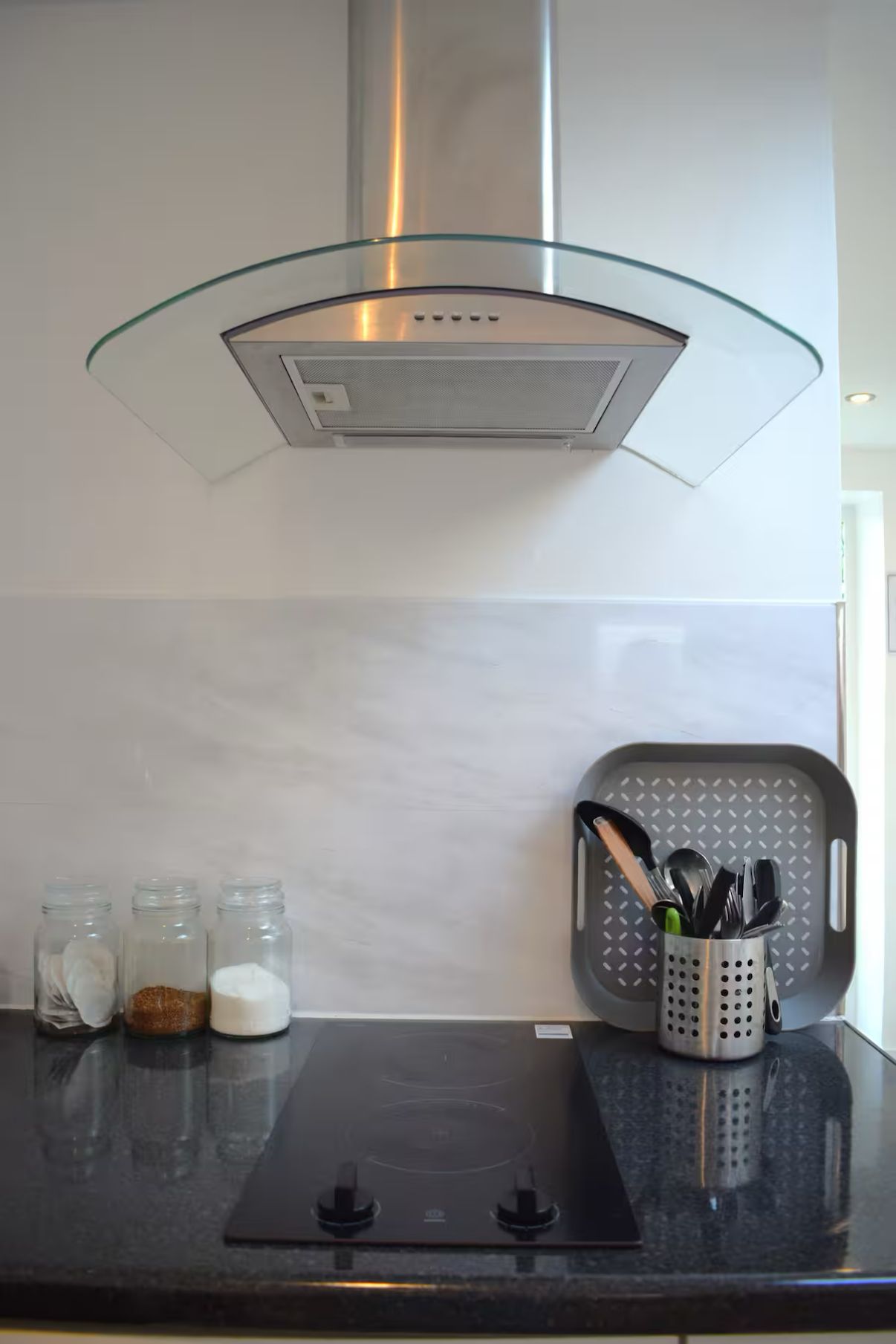 A kitchen with a glass hood, a black countertop, and jars of spices.