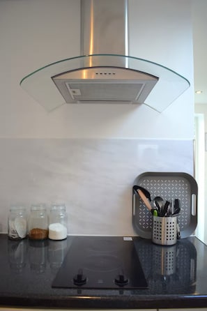 A kitchen with a glass hood, a black countertop, and jars of spices. - Delightful studio apartment close to Heathrow (Northolt)