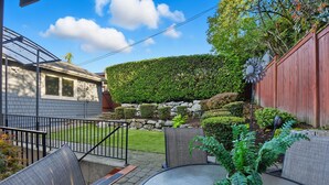 A patio area with a round table and chairs, a potted fern, and a stone wall with a hedge. - Private Guest Suite in Beautiful Kirkland, West of Market neighborhood. (Kirkland)