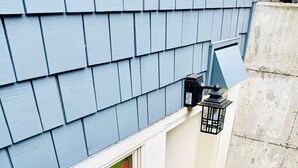 A corner of a building with a blue shingled exterior, a white door, and a window with a green curtain. - Private Guest Suite in Beautiful Kirkland, West of Market neighborhood. (Kirkland)