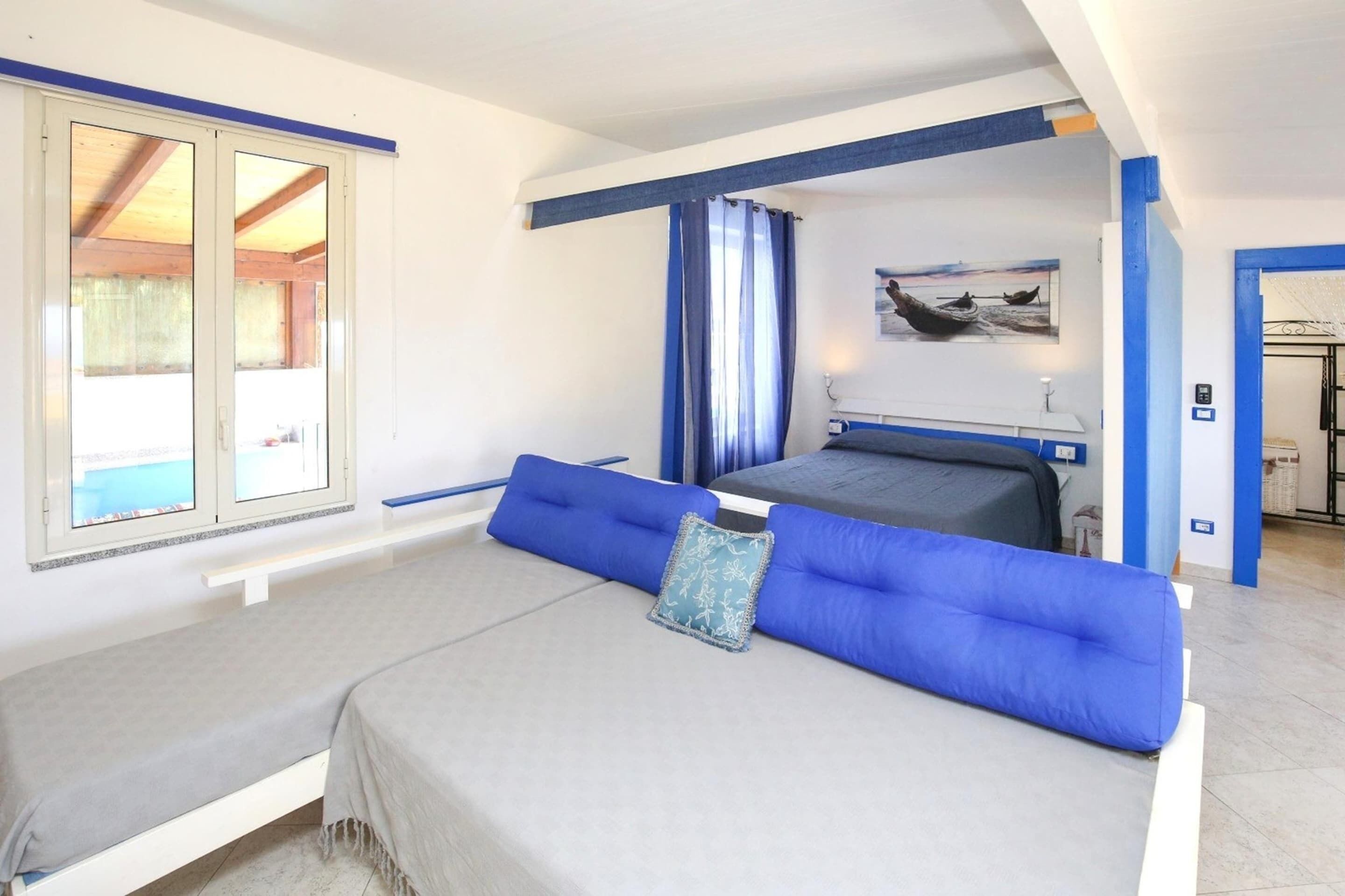 A bedroom with a bed, a window, a painting, and a bathroom door.