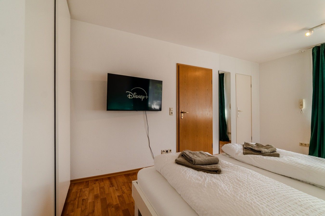Une chambre d’hôtel avec un lit, un téléviseur fixé au mur, une porte en bois et un miroir.