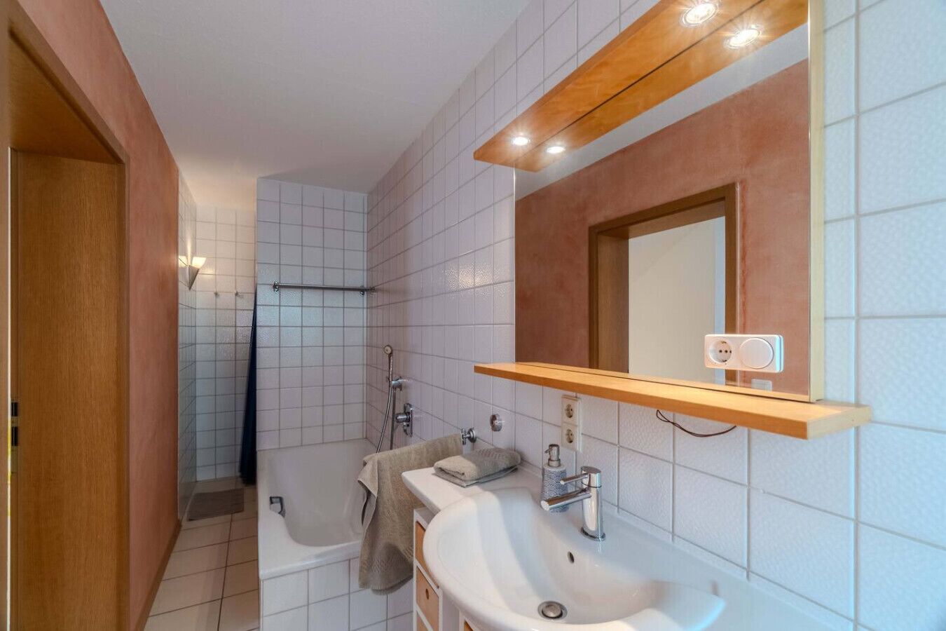 Ein modernes Badezimmer mit Dusche, zwei Waschbecken, einem Spiegel und einem Holzregal.