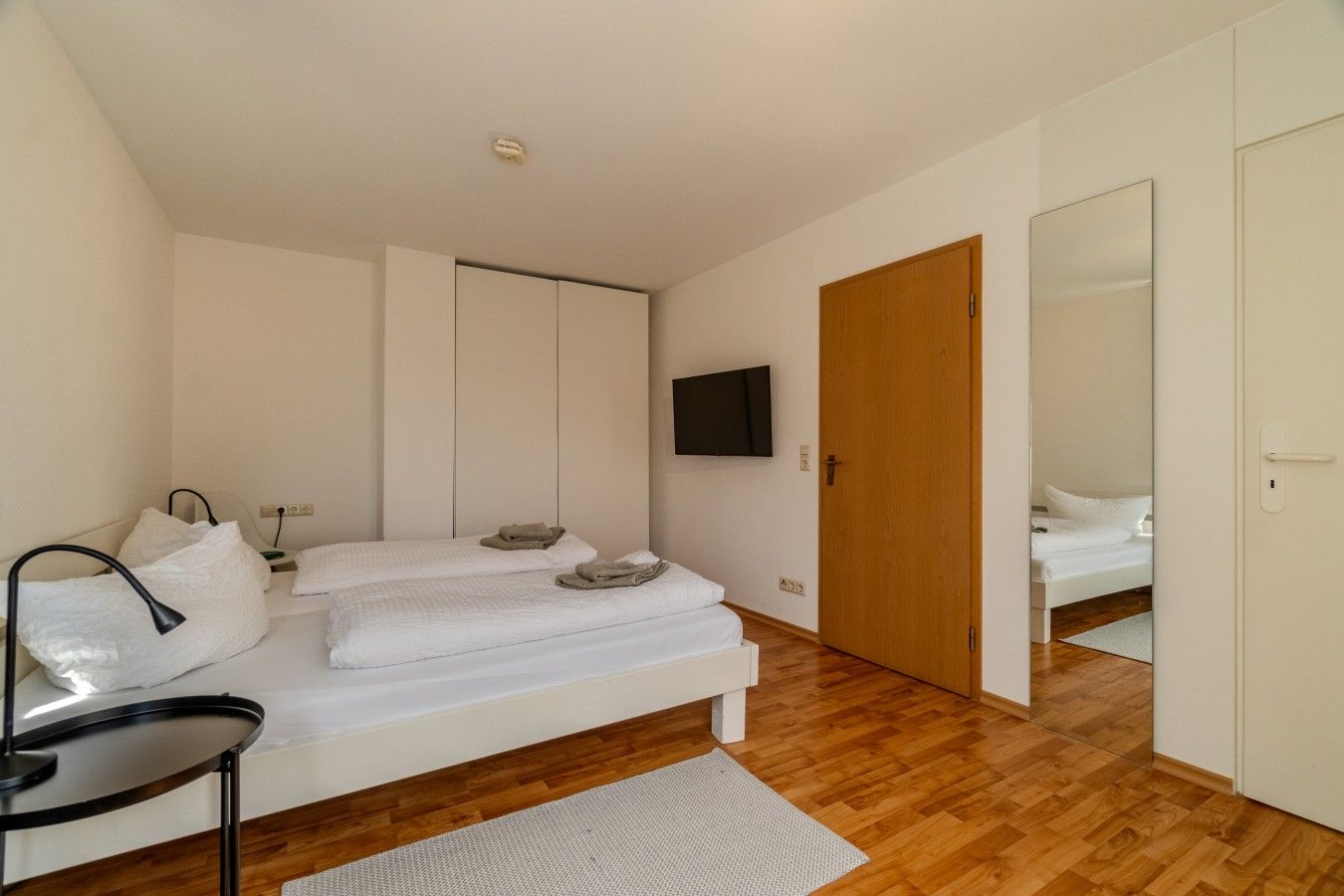 Ein modernes Schlafzimmer mit Bett, Nachttischen, einem Fernseher und Holzboden.