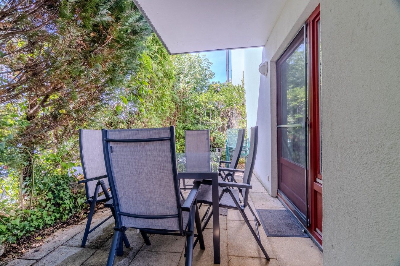 Eine Terrasse im Freien mit Tisch und Stühlen, umgeben von viel Grün.