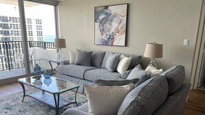 Un salon moderne avec un canapé gris, une table basse en verre et un tableau au mur.